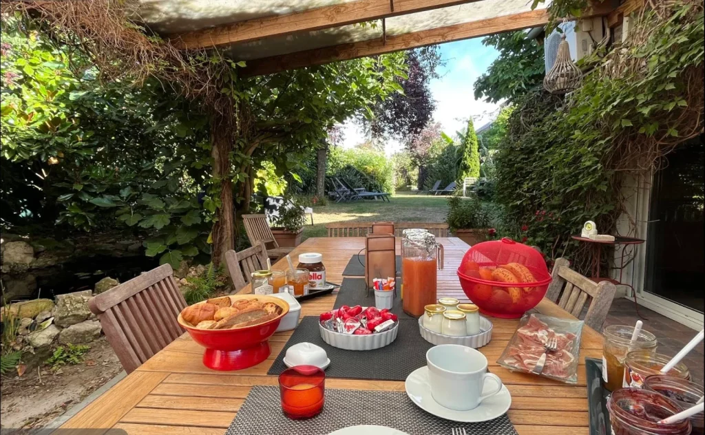 Petit-déjeuner servi sur la terrasse du Clos de Royaucourt : viennoiseries, confitures maison, jus de fruits et jambon face au jardin