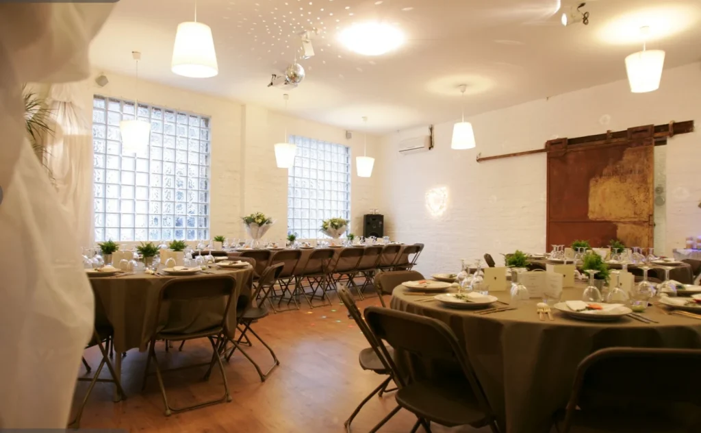 Salle de réception du Clos de Royaucourt dressée pour un événement, tables rondes et éclairage chaleureux.